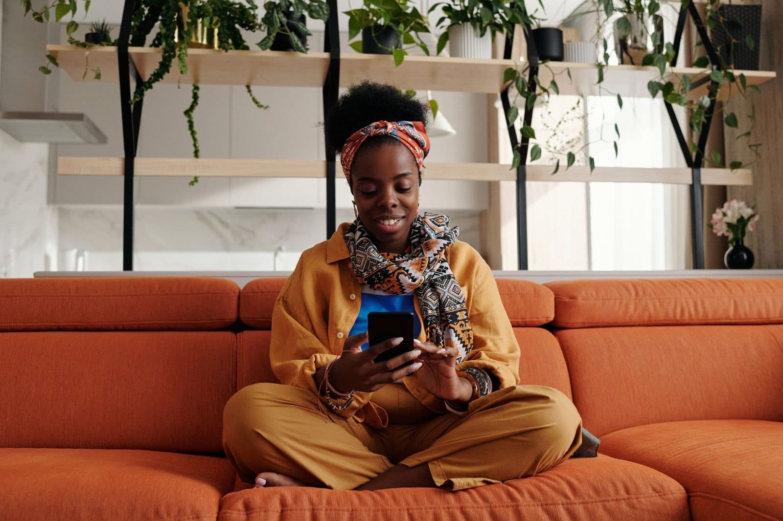 A smiling woman on an orange sofa reading her phone